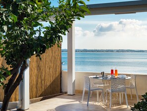 A terrace with a table and chairs overlooking a body of water, a bamboo fence, and a clear sky. - Belvilla by OYO Baia del mar (Ispica)