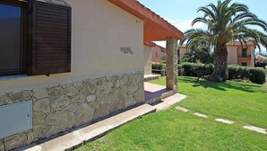 Un edificio con fachada de piedra, techo rojo y un césped bien cuidado con palmeras.
