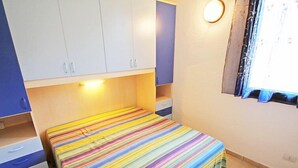 Un dormitorio con cama, armario, mesita de noche y ventana con cortinas.