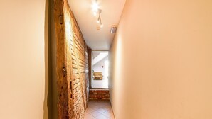 A hallway with a brick wall, a ceiling light, and a glimpse of a room with a chair. - Rustic Estate With Sauna (Nassogne)