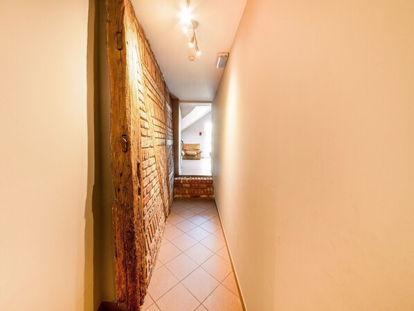 A hallway with a brick wall, a ceiling light, and a glimpse of a room with a chair. - Rustic Estate With Sauna (Nassogne)