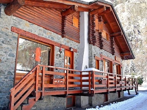 Une cabane en rondins avec une façade en pierre, un balcon en bois et une cheminée.