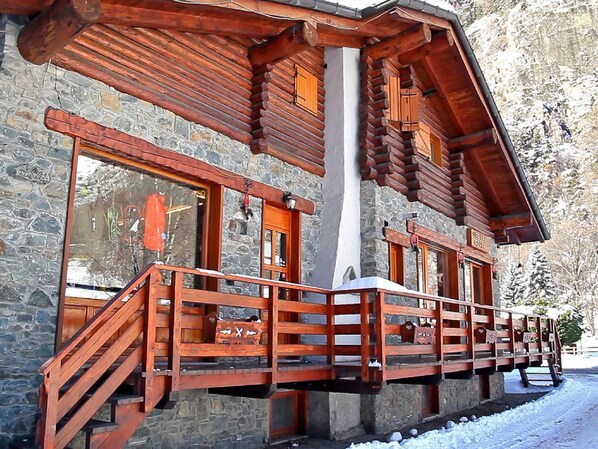 A log cabin with a stone exterior, wooden staircase, and a balcony.