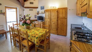 A kitchen with wooden cabinets, a dining table with chairs, a stove, and a television. - Alpine Bliss: A Cosy Retreat (Antey-Saint-Andre)