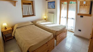 A room with two wooden beds, a window with curtains, a painting on the wall, and a wooden ceiling. - Alpine Bliss: A Cosy Retreat (Antey-Saint-Andre)