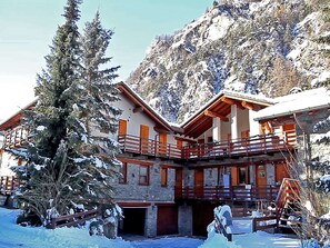 A chalet-style building with a wooden balcony, surrounded by snow-covered trees and mountains. - Alpine Bliss: A Cosy Retreat (Antey-Saint-Andre)