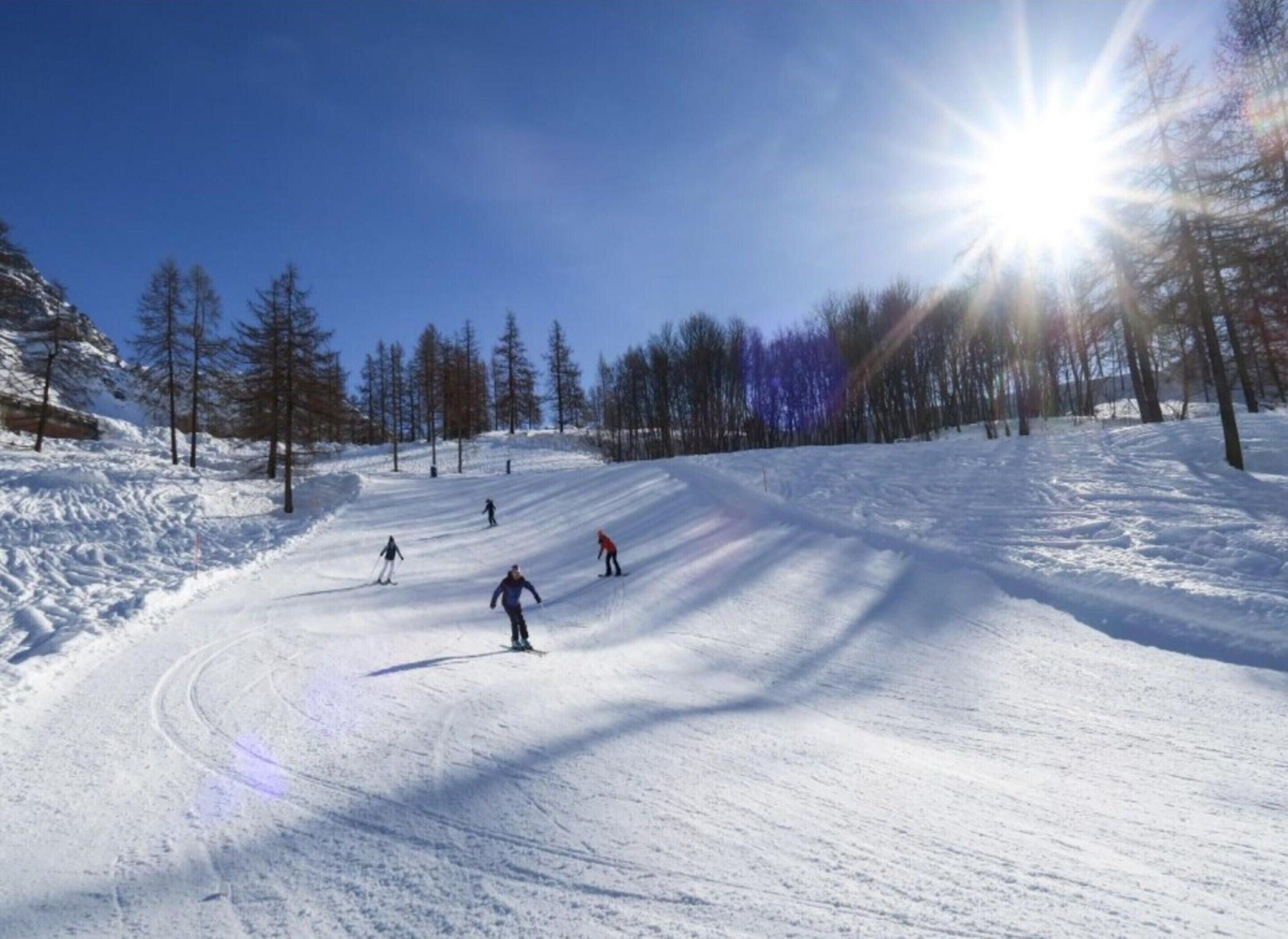 Pista de esquí nevada con esquiadores y cielo despejado.