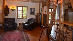 A rustic interior with wooden beams, leather chairs, a patterned rug, and a hanging light fixture.