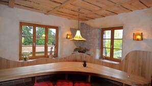 A wooden bench with red cushions, a stone wall, and two windows with wooden frames.