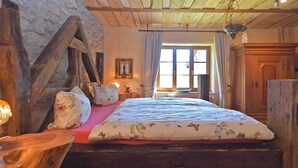 A rustic bedroom with a wooden bed, stone walls, and a large window.