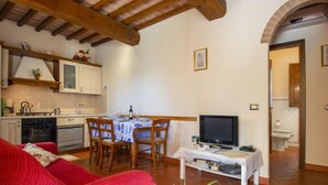 Ein gemütliches Wohnzimmer mit einem roten Sofa, einem Esstisch mit Stühlen, einem Fernseher auf einem Schrank und einer Küchenzeile mit Schränken und einem Herd.
