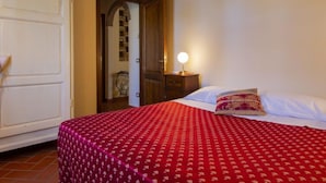 Un dormitorio con una cama, una mesita de noche con lámpara y una puerta que da a otra habitación.