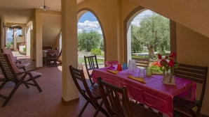 Un comedor con una mesa preparada para cuatro personas, rodeada de sillas de madera. Se observan arcos que enmarcan las ventanas y vistas a zonas verdes al exterior.