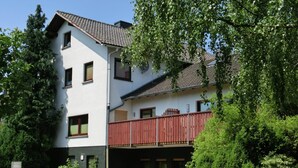 A two-story building with a balcony, surrounded by greenery. - Dog-friendly Holiday Home in Hesse With Garden (Bad Zwesten)