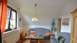 Een gezellige woonkamer met een grijze bank, een houten salontafel, een potplant en een raam met gordijnen.
