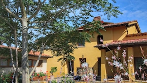 Un edificio amarillo con techo de tejas, rodeado de árboles y plantas con flores.