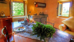 Una cocina acogedora con una mesa dispuesta para dos, que incluye un mantel de encaje, una botella de aceite de oliva y verduras frescas.