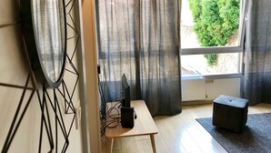 Una habitación con un escritorio de madera, un taburete negro y un amplio ventanal con cortinas.