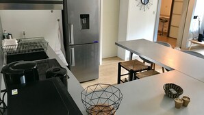 Una cocina moderna con un refrigerador de acero inoxidable, un lavamanos y un comedor con mesa y sillas.