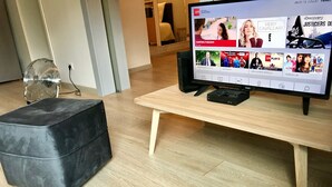 Una sala de estar moderna con un televisor de pantalla plana sobre un mueble de madera, un otoman negro y un ventilador de pie.