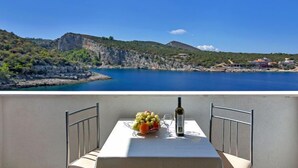 Un balcón con una mesa dispuesta para dos personas, con vista a un paisaje costero con acantilados y una extensión de agua.