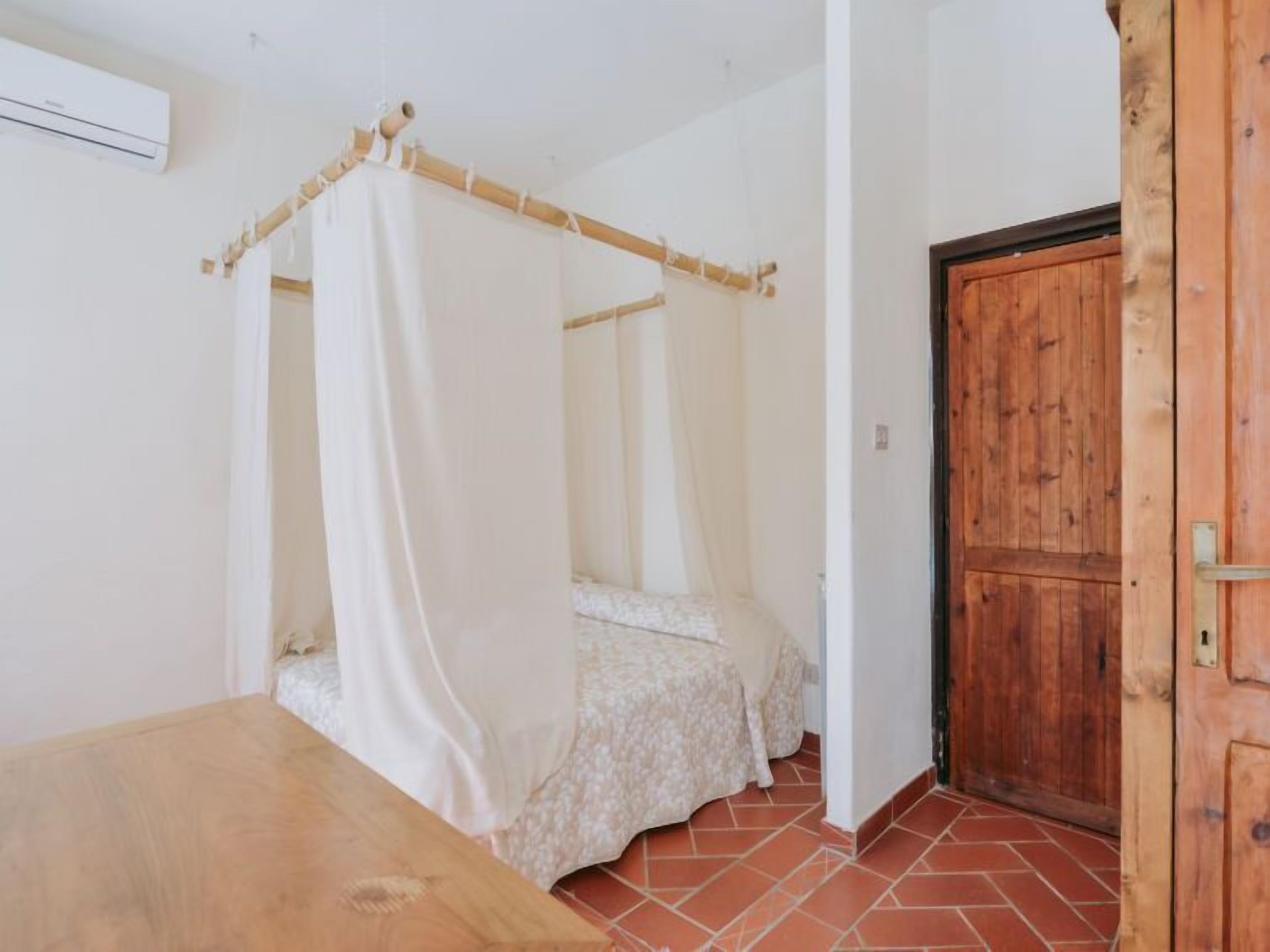 Ein Schlafzimmer mit Himmelbett, Holztür und Fliesenboden.