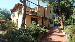 Una casa a due piani con un balcone, immersa nel verde e con un vialetto in mattoni.