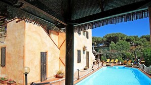 Area piscina con vasca azzurra e cristallina, circondata da lettini e piante in vaso.