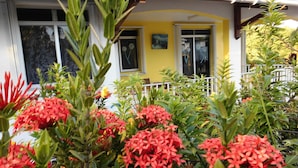 A building with a yellow facade, white windows, and a balcony with a railing. - Charming T2 '' Le Colibri '' garden floor with flowers and all comforts in Ste Anne Wifi (STE ANNE)