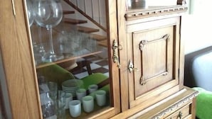 Un mueble de madera con puertas de cristal, que contiene cristalería y platos.