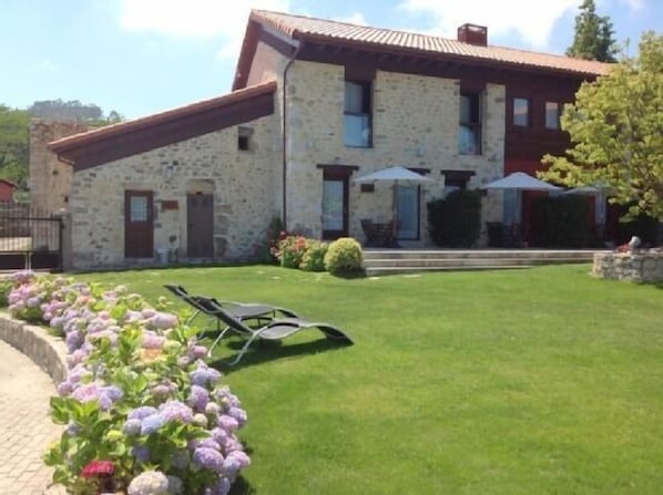 A stone building with a red roof, a small garden with flowers, and a lawn.