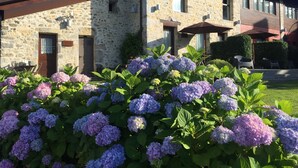 Un edificio de piedra con una puerta marrón y ventanas, rodeado de arbustos de hortensia.