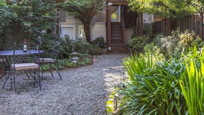 Une terrasse en gravier avec une table et des chaises, entourée d’une végétation luxuriante et d’une clôture en bois.