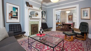Un salon avec une cheminée, une table basse en verre et un tapis rouge à motifs.