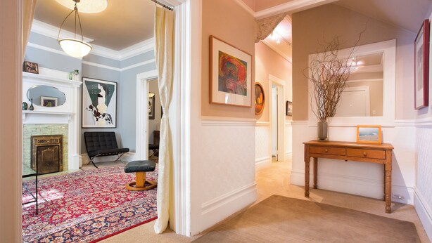 Un couloir avec un tapis à motifs, une console en bois et une œuvre d’art encadrée accrochée au mur.