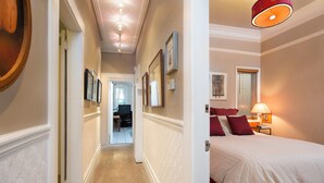 Un couloir d’hôtel avec un lit, une lampe et des tableaux encadrés accrochés au mur.