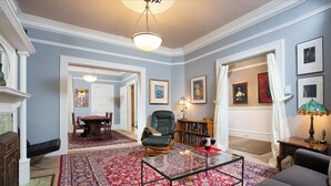 Un salon avec une cheminée, une table basse en verre, un canapé, un fauteuil, un tapis et des œuvres d’art encadrées accrochées aux murs.