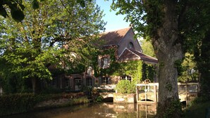 Ein historisches Gebäude mit Backsteinfassade, einer kleinen Brücke und einem Teich, der die Struktur spiegelt.
