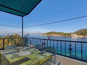 A balcony with a table set for two, overlooking a body of water and a hilly landscape.