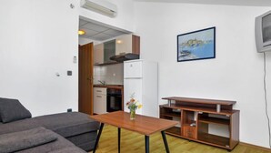 Un espacio habitable compacto con sofá, mesa de madera, área de cocina y televisor.