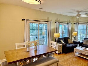 A living room with a wooden dining table, white chairs, a dark sofa, and a ceiling fan. - River and Marsh Views, Oceanfront Community, Beautiful Sunsets, Golf Cart (St Helena Island)