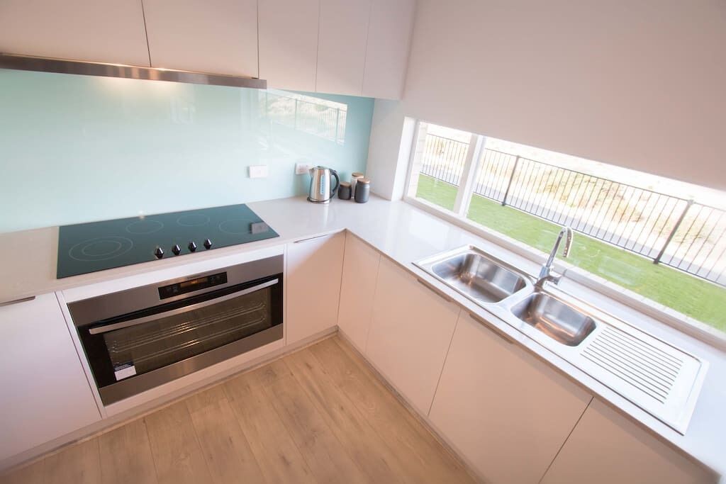 A modern kitchen with a built-in stove, oven, and a large window with a view of a green lawn.