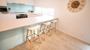 A modern kitchen with white cabinets, a large island with bar stools, and a wooden wall clock. - 'Serenity' and sweeping Murray River views (Tailem Bend)