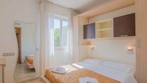 Une chambre d’hôtel comprenant un lit, un grand miroir, une fenêtre avec des rideaux et une étagère intégrée pour la télévision.