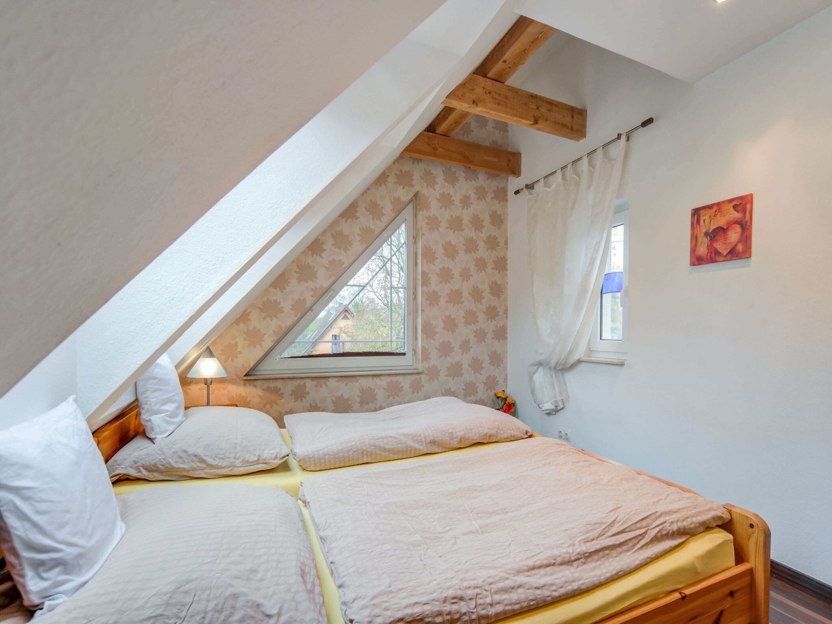 Un dormitorio con techo inclinado, una ventana con vistas, una cama con dos almohadas y una mesita de noche.