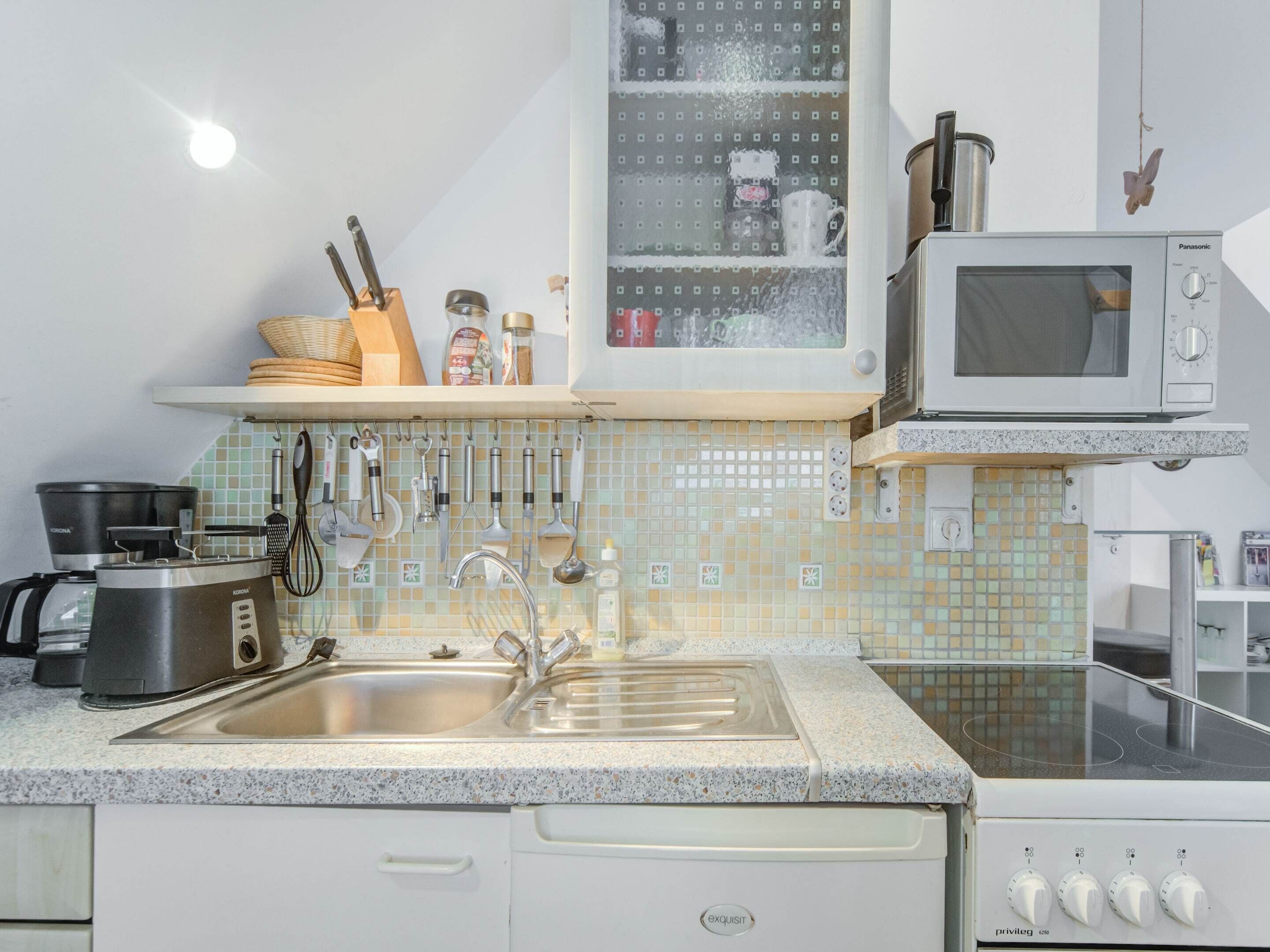 A kitchen with a sink, stove, microwave, and various utensils.