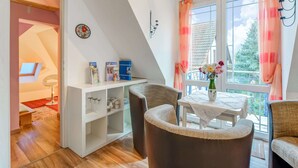 Une pièce chaleureuse avec un plafond en pente, une table à manger avec des chaises, une bibliothèque et une fenêtre avec des rideaux.