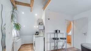 Une cuisine moderne avec un réfrigérateur, un four à micro-ondes et une cuisinière, tous de couleur blanche. On y trouve deux tabourets de bar et une plante en pot.