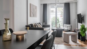 Ein modernes Wohnzimmer mit Essbereich, grauen Sofas, einem Couchtisch und einem an der Wand befestigten Fernseher.
