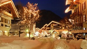 Un village enneigé, avec des bâtiments illuminés et un arbre au centre.